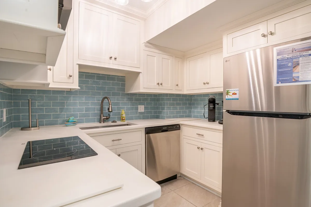 A modern, well-equipped kitchen featuring a blue tiled backsplash, stainless steel appliances, and bright white cabinetry. The layout is open and inviting, with ample countertop space for preparing meals or entertaining guests. The scene conveys a sense of culinary opportunity and gathering.