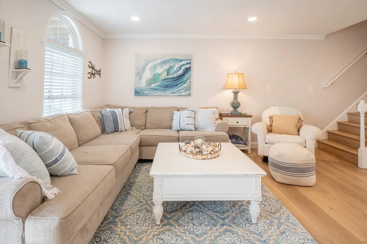 A spacious interior living area with a large sectional sofa, coffee table, ocean-themed artwork, and a table lamp, ideal for hosting game nights or relaxing together after a meal.