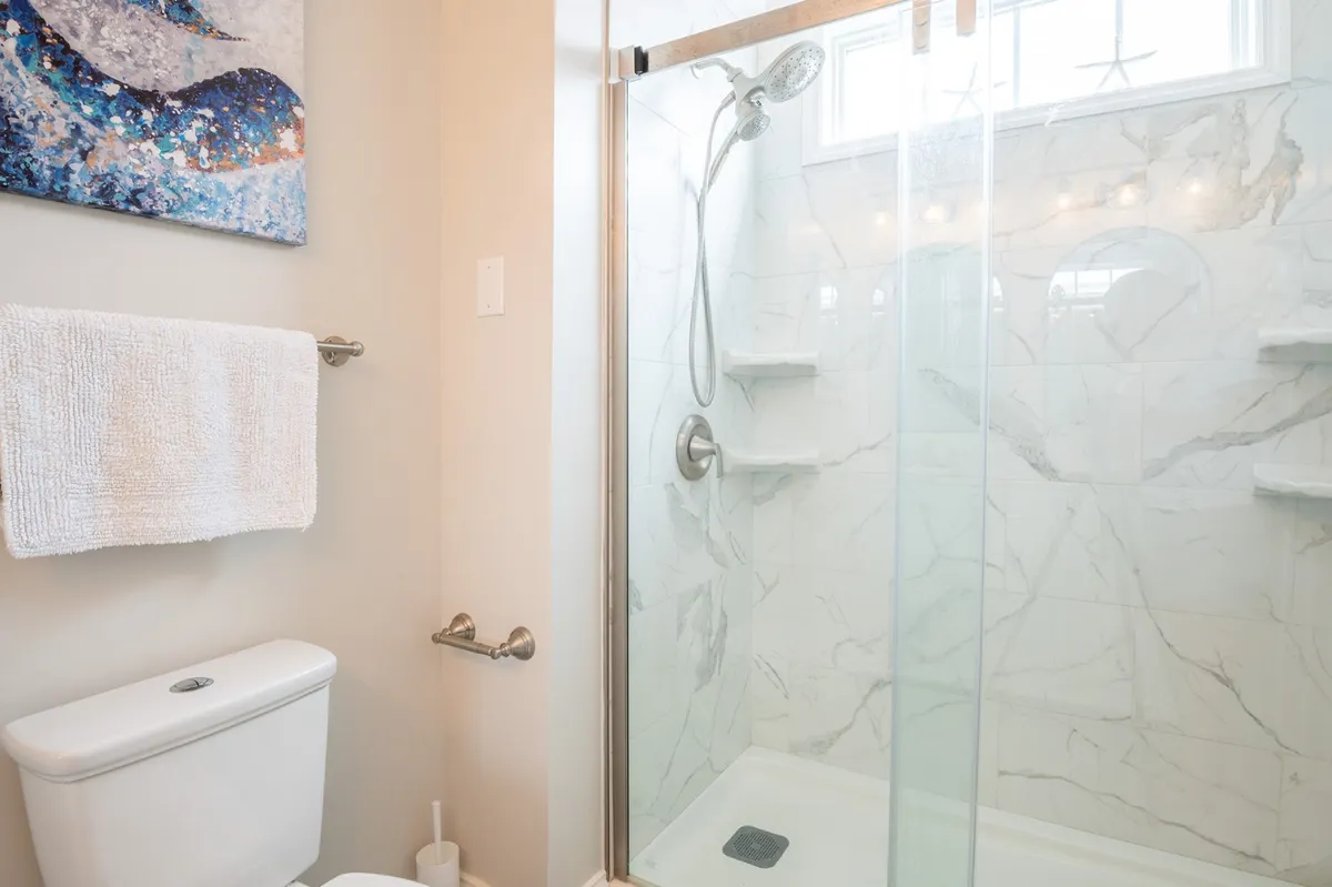 A luxurious bathroom featuring modern fixtures, marble tiles, a glass-enclosed shower, and colorful artwork. The room is bright, tranquil, and evokes a spa-like sense of relaxation.