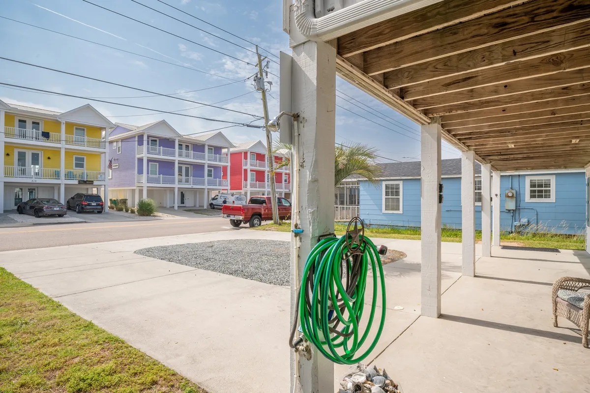 A cheerful exterior view featuring a row of colorful buildings, a green garden hose, and a gravel area surrounded by greenery. The space suggests an inviting outdoor environment perfect for relaxing or socializing, with hints of communal activity in a sunny setting.