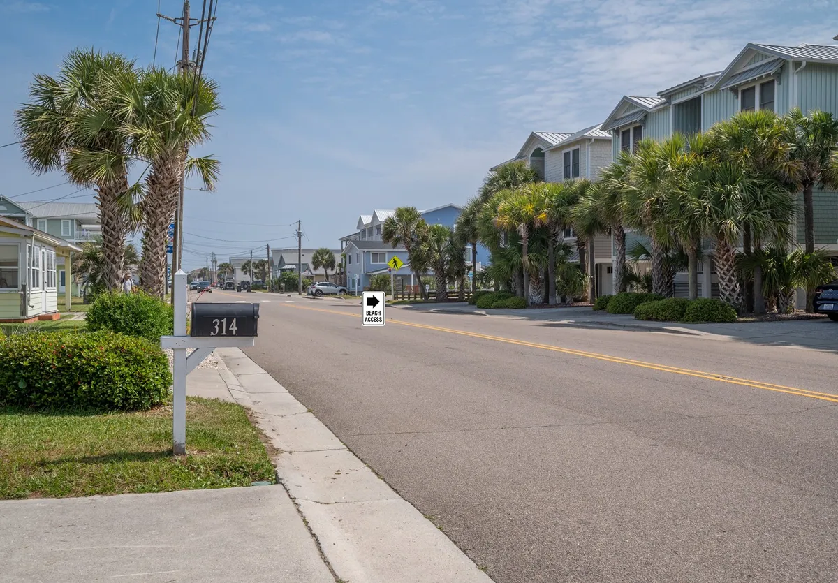 A relaxed neighborhood street scene featuring a prominent mailbox marked 314, swaying palm trees, and a backdrop of residential buildings. The perspective hints at a walkable, inviting locale where locals and visitors can stroll, bike, or socialize. The natural light and open sky evoke a sense of easy access to community activities and nearby attractions.