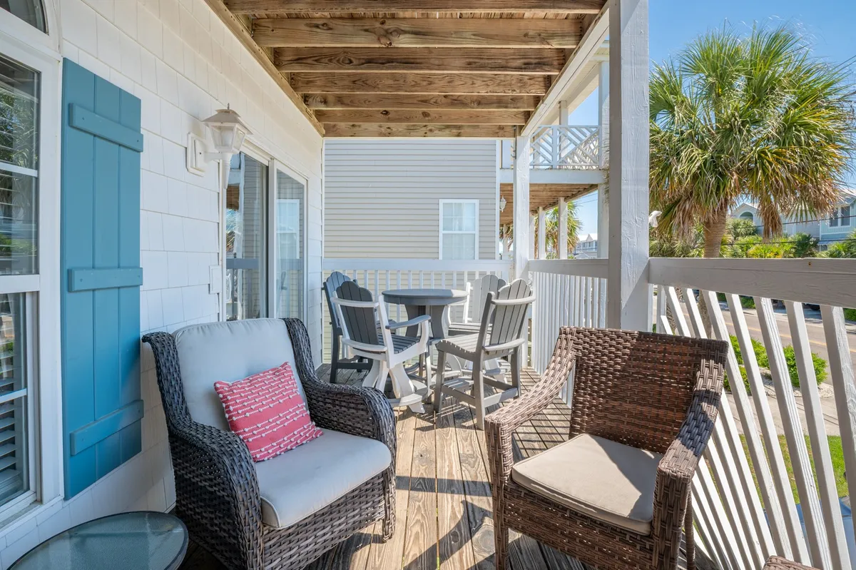 An exterior patio space featuring wicker chairs, a wooden table, blue shutters, and palm trees, perfect for relaxing, enjoying meals outdoors, or having conversations in the fresh air.