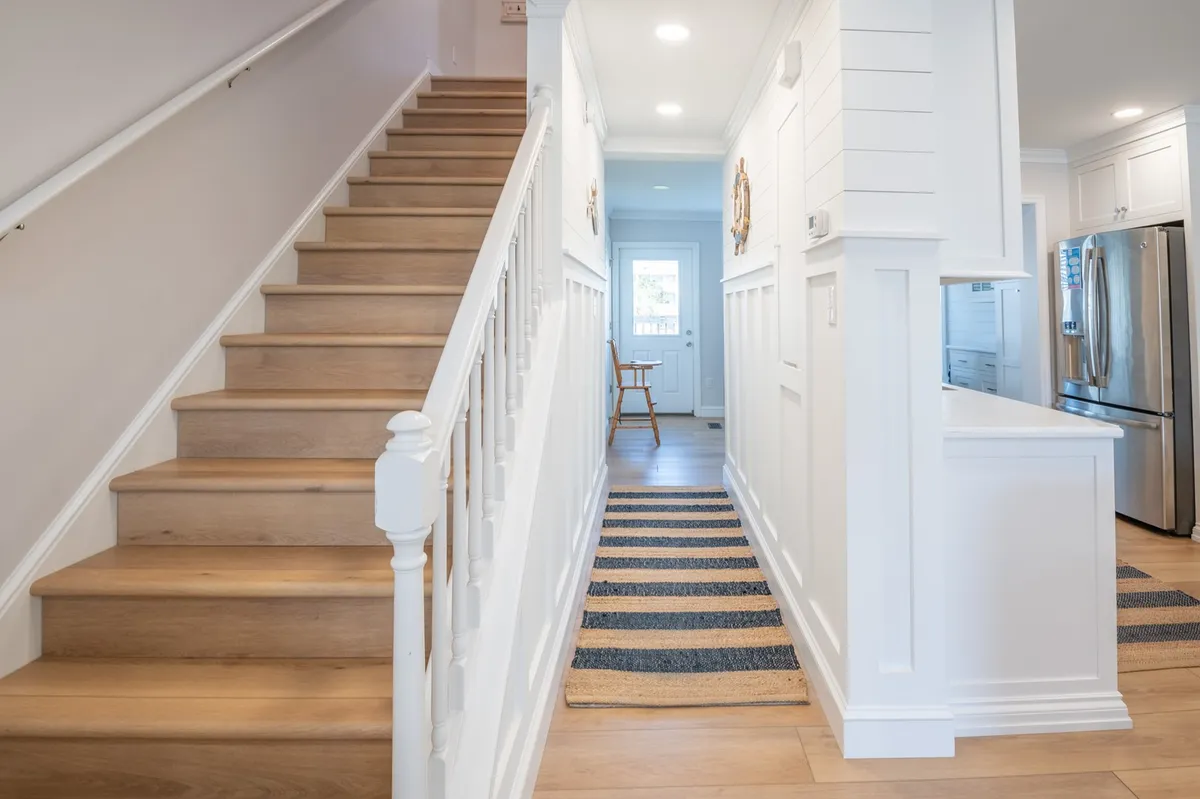 A warm view of the staircase leading to a kitchen entrance, featuring a blue-striped runner rug that ties the spaces together. The scene feels both homey and transitional, capturing the sense of moving between private and shared areas.